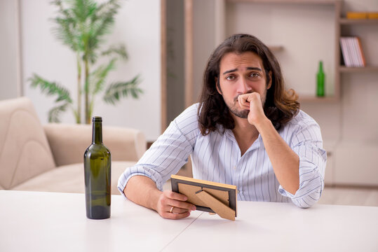 Young man drinking alcohol at home in unhappy love concept