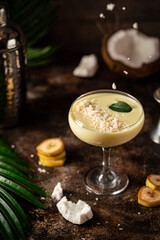 banana cocktail with coconut milk in a glass on dark background with palm leaves