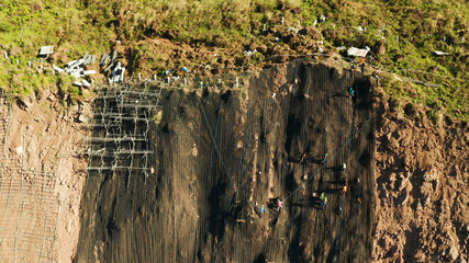 Workers strengthen the slope of the mountain with metal mesh preventing rockfall and landslide on the road, above view. workers constructing anti-landslide concrete wall prevent protect against rock