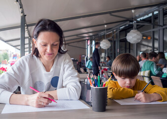 Mom and son is playing Sea Battle at street cafe. Family games. Strategy type guessing game for two players.