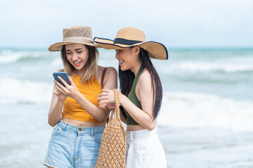 Two Asian girl friends wearing hats for a walk on the beach using their smartphones to check in Beach locations on social networks 