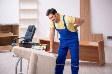 Young male carpenter repairing arm-chair in the office