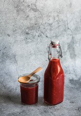 Obraz premium Rhubarb and strawberry sweet sauce in a canned bottle on a gray background. Free space for text