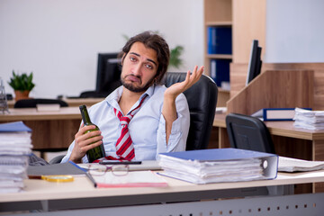 Young male employee drinking alcohol in the office