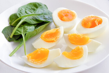 Boiled eggs with spinach leaves on a white plate. 