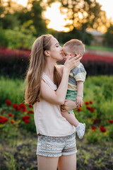 Obraz premium A young beautiful mother kisses and hugs her little son during the sunset in the park. Happy family walk in the park.