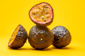 Fototapeta na wymiar Arrangement of Maracuja or Brazilian tropical passion fruit studio food still life against a yellow background cut open with black seeds and pulp flesh showing
