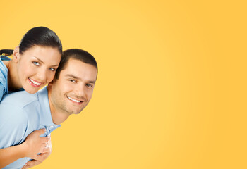 Happy amazed smiling couple. Portrait of standing close embracing models in love studio concept, isolated over orange yellow colour background. Young brunette man and woman together. Copy space area.