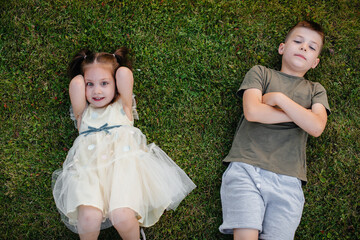 Brother and sister run, play and have fun on the grass in the park on a summer day during sunset. Happy childhood.