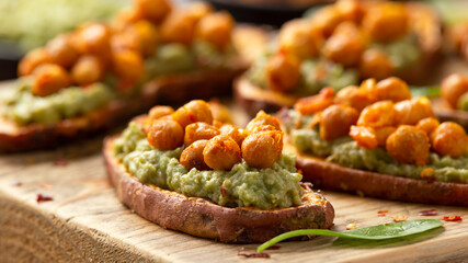 Sweet potato toast loaded with avocado guacamole and baked chickpeas sprinkled with chili flakes served on wooden board