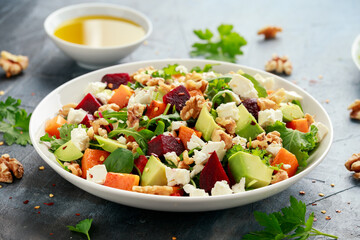 Healthy Butternut squash salad with beetroot, avocado, walnut and feta cheese in white bowl