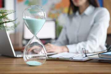 Glass hourglass standing against background of woman working at laptop closeup