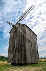 Old abandoned wooden mill and wheat summer field