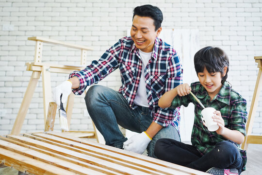 Woodwork and people concept. Little Boy is learning to work on wood. Father and son working with wood plank in workshop. Father and son painting on wood.