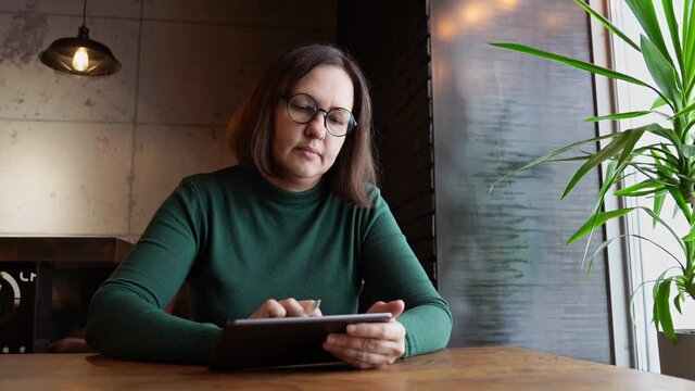 Pretty woman sitting in cafe and working. Green dress with long sleeves. Casual lifestyle portrait. Business female person draw with pencil. Vlog slow video. Wide