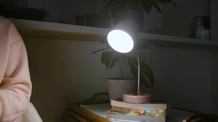 A small lamp flickers with possible power outage as a woman sits next to it