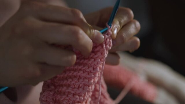 Extreme close up of woman's hands knitting a pink piece of clothing.