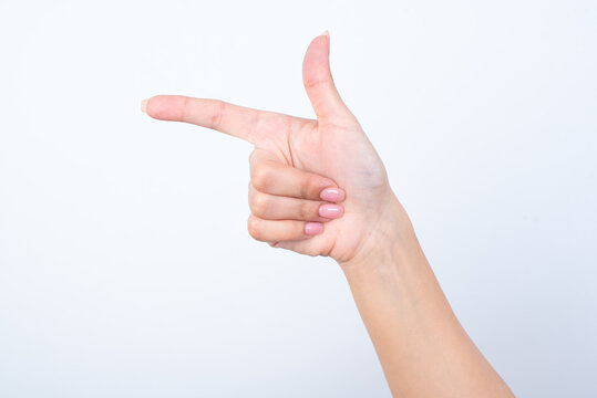 Woman's hand with pink manicure over isolated white background  pointing aside with forefinger or imitating a gunfire. 