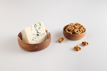 Obraz na płótnie Canvas Portion of blue cheese with walnuts, white table background, wooden bowls.