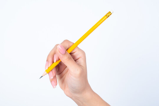 Woman's hand with pink manicure holding a yellow pencil over white studio background.
