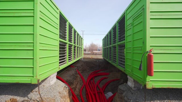 Modular bitcoin mining farm construction site. ASIC mining equipment in green steel shipping containers. Installing powerful server blockchain datacenter. Electrical power cables in trench.