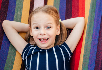 Happy little girl with crooked baby teeth in the colorful hammock summer background, summer holiday...