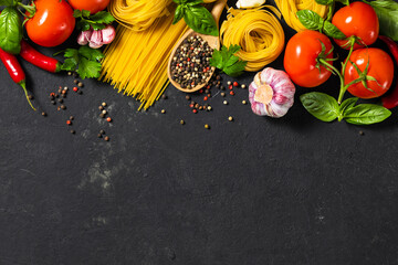 Italian food ingredients with pasta, tomatoes, pepper, garlic and parsley on dark background with copy space, top view