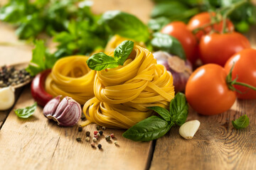 Tagliatelle on wooden table with basil leaf, pepper, garlic and parsley close up with copy space, Italian food ingredients