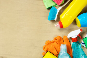 Various cleaning supplies, sprays, bottles, sponge, rubber gloves on wooden background with copy...
