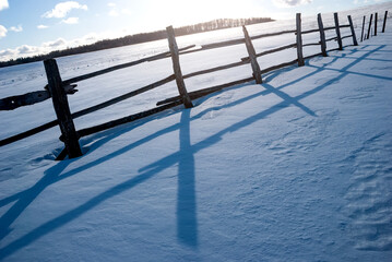 Winter landscape. Fence in snowdrifts against the background of the forest and the sun.