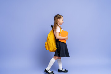 Cute happy kid in uniform. raises his leg high and runs on purple background. child with backpack. little girl is ready for school. Dynamic images that go back to conceptual school. holidays begin.
