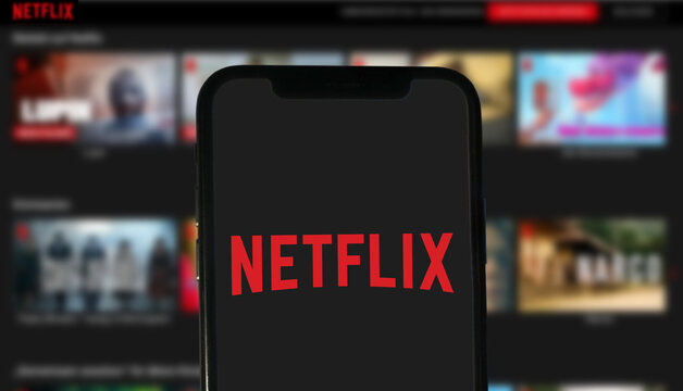 Netflix Logo wird auf einem modernen Smartphone angezeigt, im Hintergrund wird eine Auswahl an Serien und Filmen der Streamingplattform angezeigt, 2021