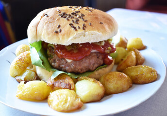 Homemade cheeseburger with potatoes on a white plate a dinning room