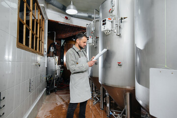 A young bearded brewer monitors the sensor readings during the brewing process. Making beer.