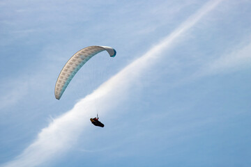 white paraglider flying in blue sky with line of clouds