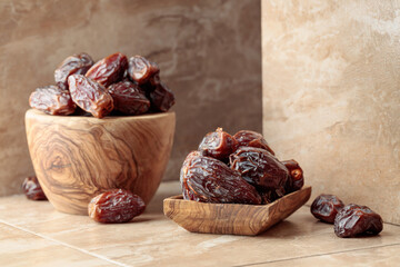 Dates fruit in a wooden dish on a beige ceramic table.