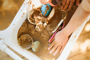 Happy children play with sand and water in sensory baskets on the outdoor sensory table, sensory early development, montessori. Baby hands with sand and water close up, soft focus