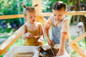 Happy sister kids play with sand and water in sensory baskets on the outdoor sensory table, sensory...