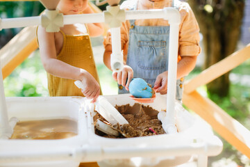 Happy sister kids play with sand and water in sensory baskets on the outdoor sensory table, sensory...
