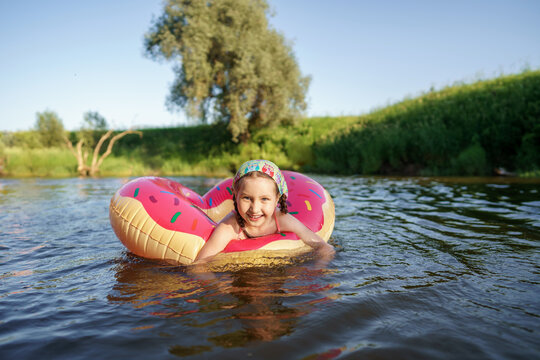 Happy girl in swimming glasses swims on an inflatable circle in the river in summer at sunset. A child enjoys a summer children's holiday on the shore of the lake. Active holidays. Dynamic image