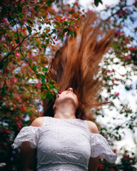 Naklejka premium A model with long hair in a park. A blooming garden. The hair develops beautifully.