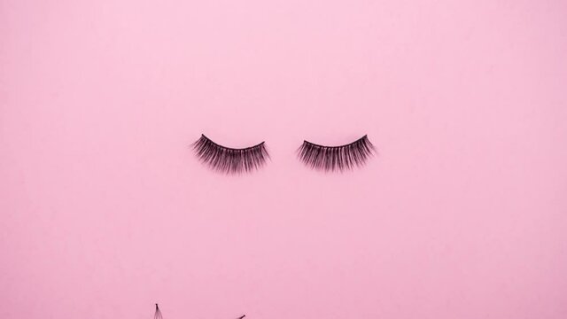 Lashes loss and extension concept. Fake eyelashes fall on trendy pastel pink background. Makeup accessories. Cosmetic products. Stop motion animation. Beauty pattern.