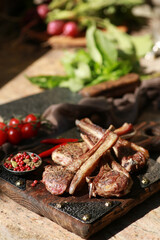 Grilled lamb ribs with spices and fresh vegetables and herbs on a wooden board. Picnic, outdoor, sunlight,a square of lamb. Rustic. Background image, copy space