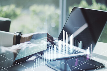 Abstract creative financial graph with hand typing on laptop on background, forex and investment concept. Multiexposure