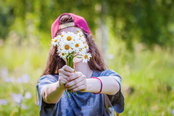 Teenage girl in cap holds bouquet of flowers and covers her face. Modern concept of anonymity