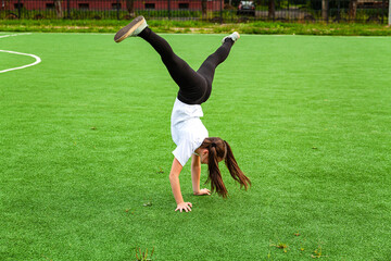 The girl is engaged in acrobatics in the stadium. Warm-up, stand-up, child, street, day