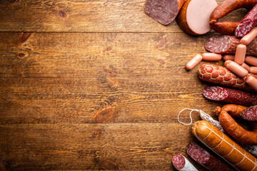 Set of different types of sausages, salami and smoked meat with basil and spices on wooden background. Top view.