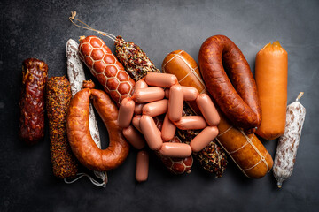 Set of different types of sausages, salami and smoked meat with basil and spices on a black...
