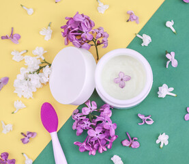 Obraz na płótnie Canvas Face cream, lilac and mask brush. Face cream, lilac flowers and a brush for masks lie on a yellow-green background, close-up top view. 