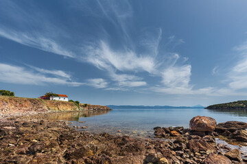 Mediterranean landscape with a small bay and a lonely house with whitewashed walls and a red tiled roof under a clear blue sky with light clouds